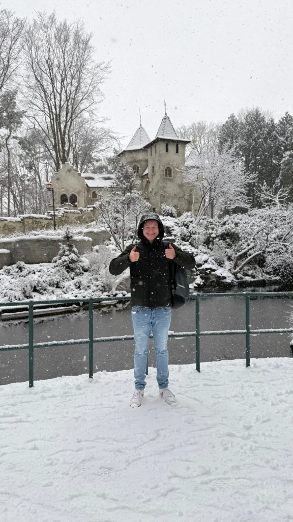 Sietse glimlachend in de sneeuw met twee duimen omhoog voor een magisch, besneeuwd kasteel